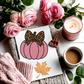 Pink pumpkin with leopard print bow card on a surface with pink roses, a candle, and coffee.