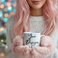 Person with pink hair holding a mug with 'Your Design' text against a blurred festive background